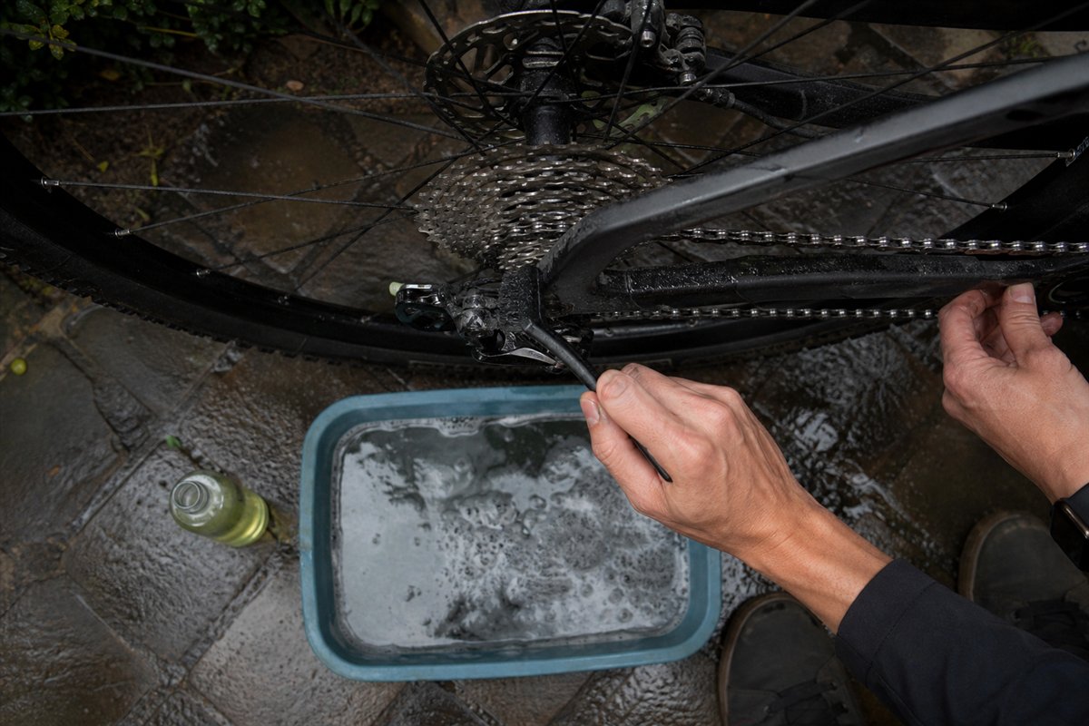 A muddy bicycle drivetrain being cleaned carefully with a brush