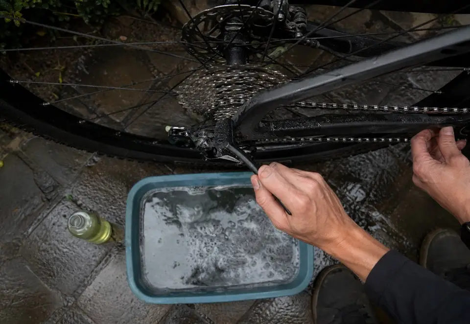 A muddy bicycle drivetrain being cleaned carefully with a brush